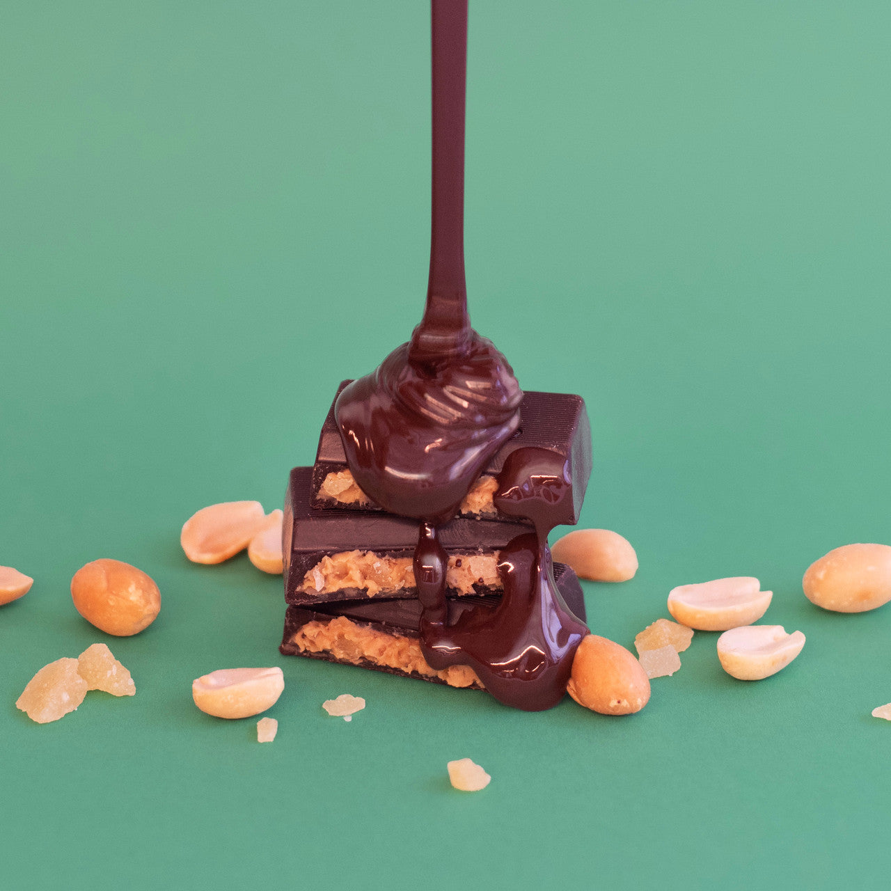 Chocolate being poured over a peanut butter bar with peanuts on a green background
