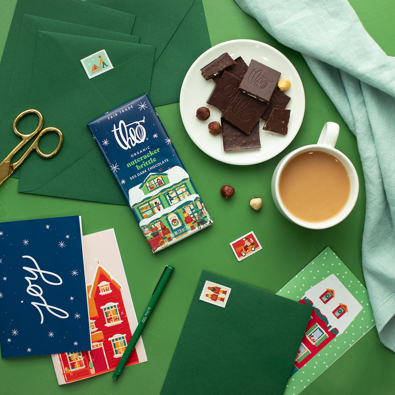 Chocolate bars, a cup of coffee, and holiday-themed stationery on a green surface
