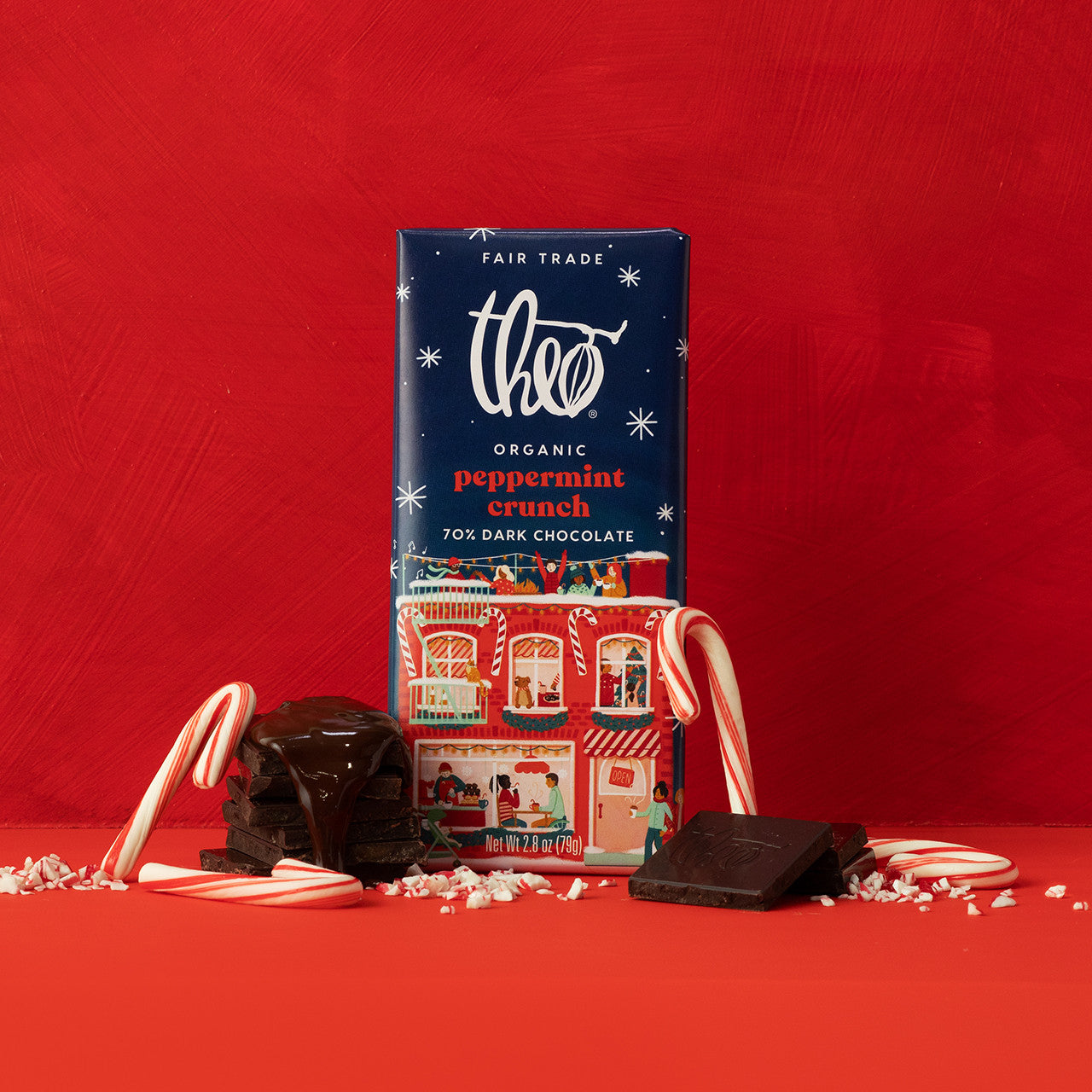 Theo Organic Peppermint Crunch chocolate bar packaging on a red background with candy canes and chocolate pieces.