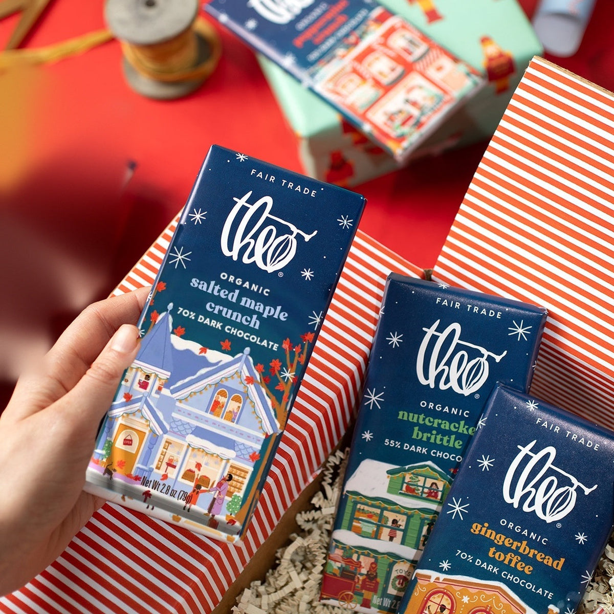 Hand placing a Salted Maple Crunch bar into a holiday gift box with other Theo holiday bars