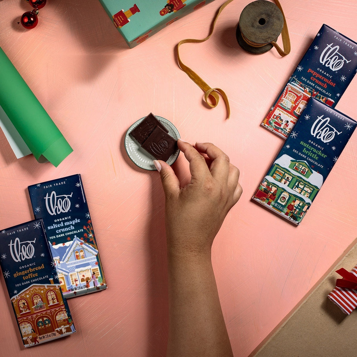 Hands breaking a square of Theo chocolate during late night gift wrapping, holiday bars nearby