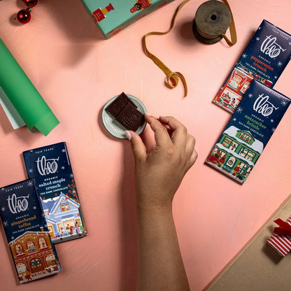 Hands breaking a square of Theo chocolate during late night gift wrapping, holiday bars nearby