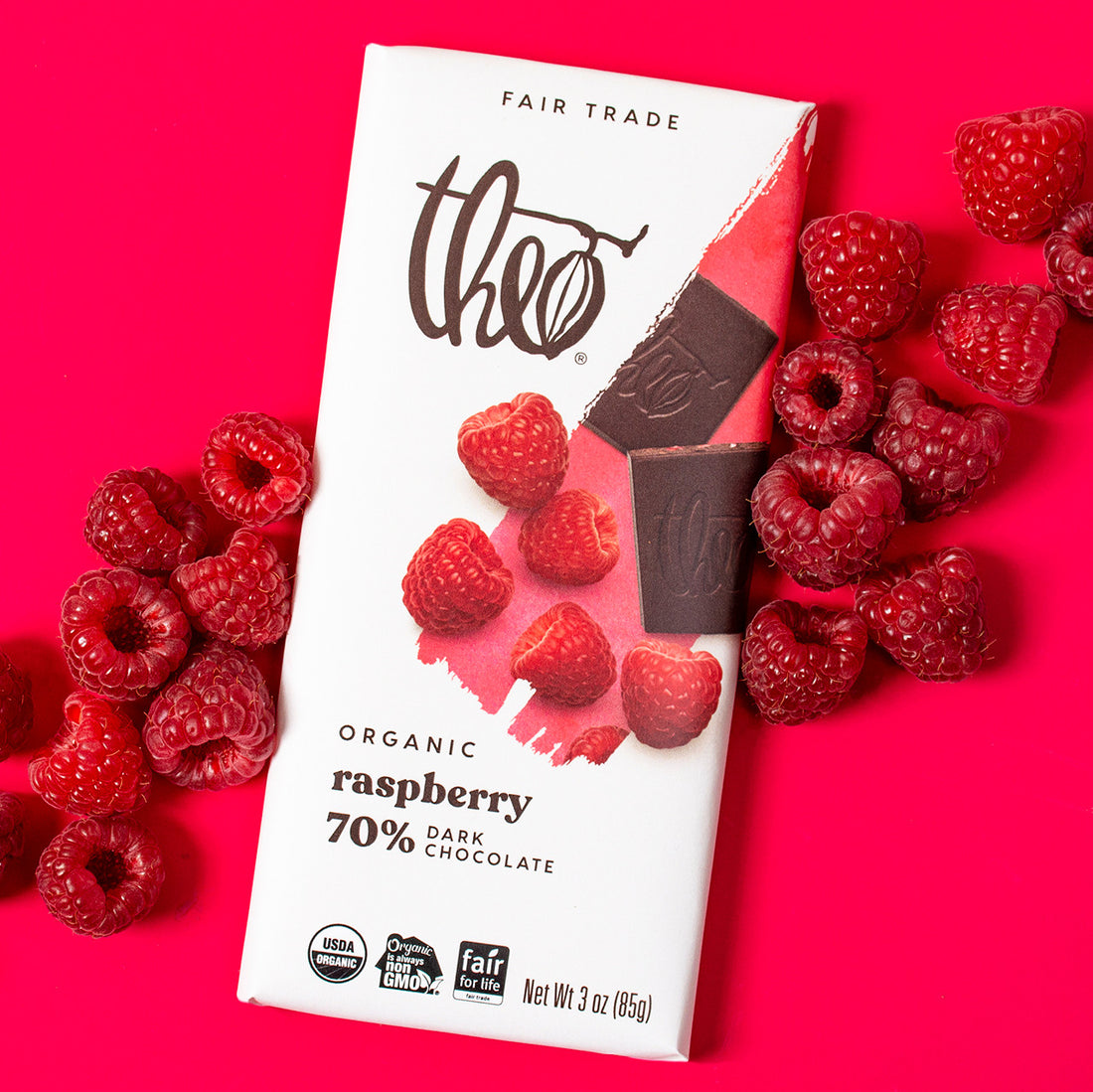 Theo Organic Raspberry 70% Dark Chocolate bar with raspberries on a pink background