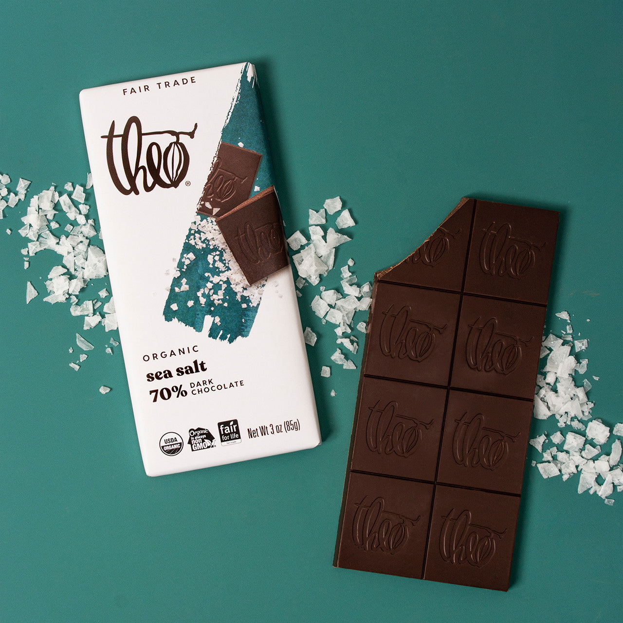 Theo Organic Sea Salt 70% Dark Chocolate bar with packaging on a teal salt covered background