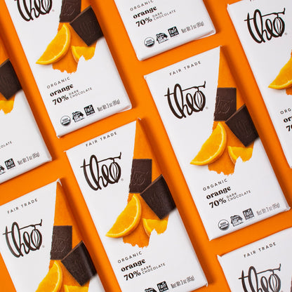 Theo Organic Orange 70% Dark Chocolate bars with orange slices and chocolate pieces on a white background.