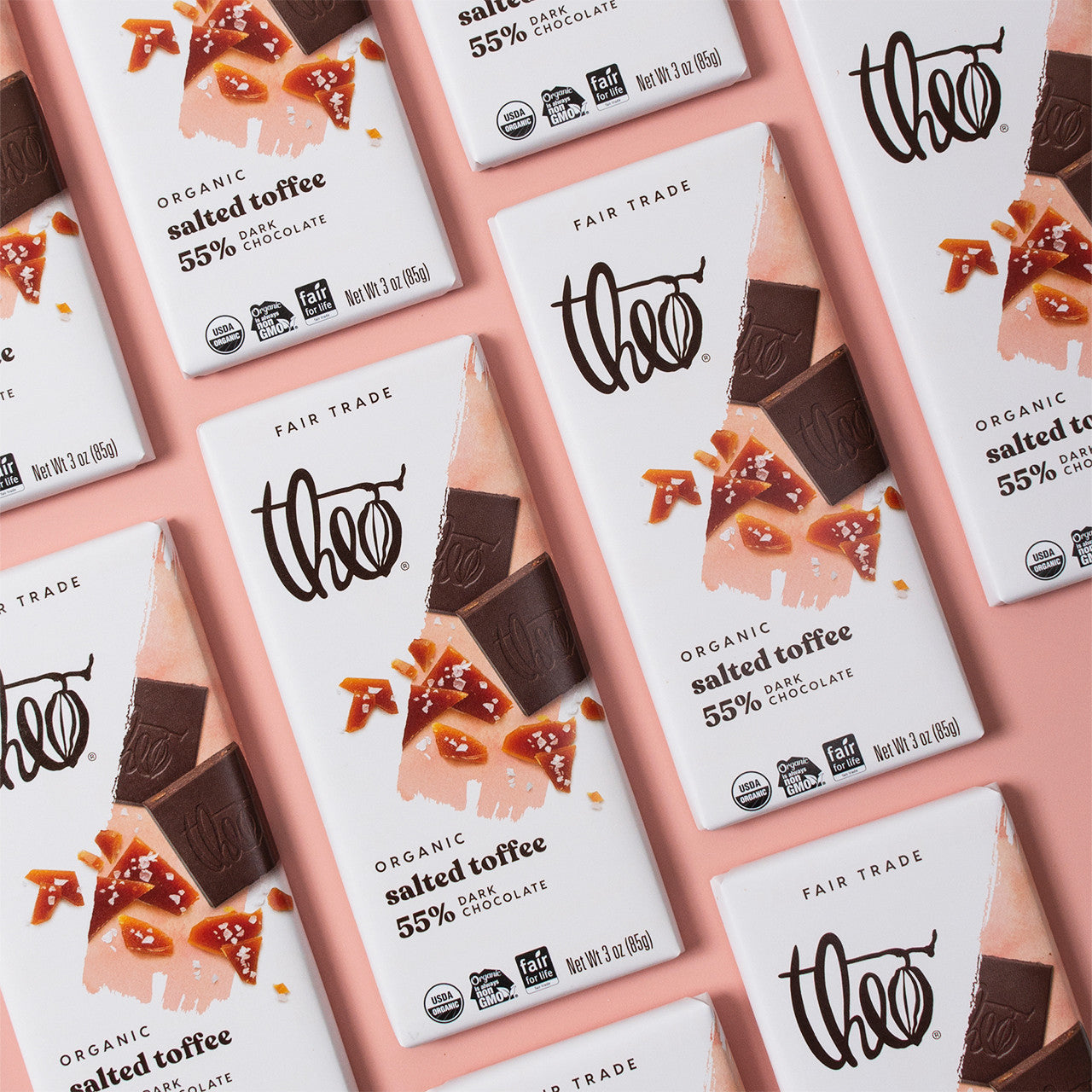 Multiple Theo chocolate bars with salted toffee flavor packaging on a pink background