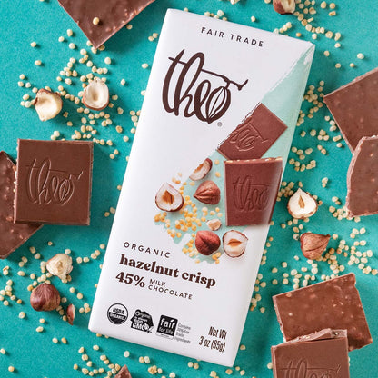 Theo Organic Hazelnut Crisp 45% milk chocolate bar packaging with chocolate pieces and nuts on a teal background