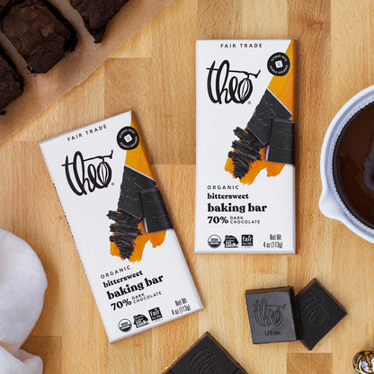 Two Theo Organic chocolate baking bars on a wooden surface with a cup of coffee and brownies.