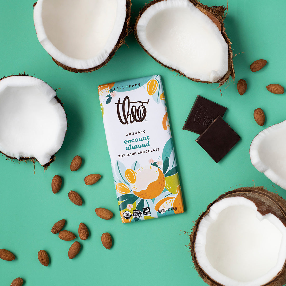 Theo Organic Coconut Almond Dark Chocolate bar surrounded by coconuts, almonds, and chocolate pieces on a green background