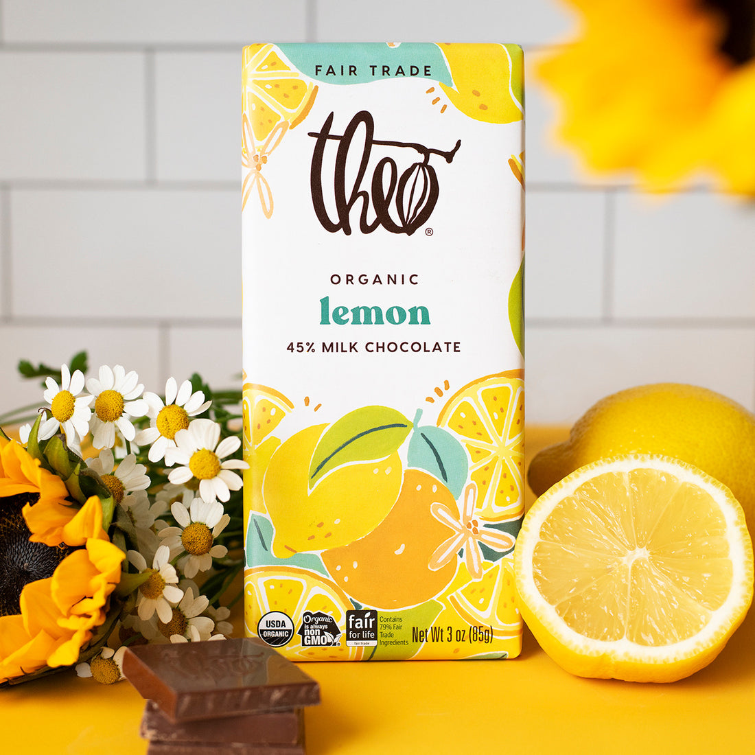 Theo Organic Lemon Milk Chocolate packaging with lemons and flowers on a yellow surface