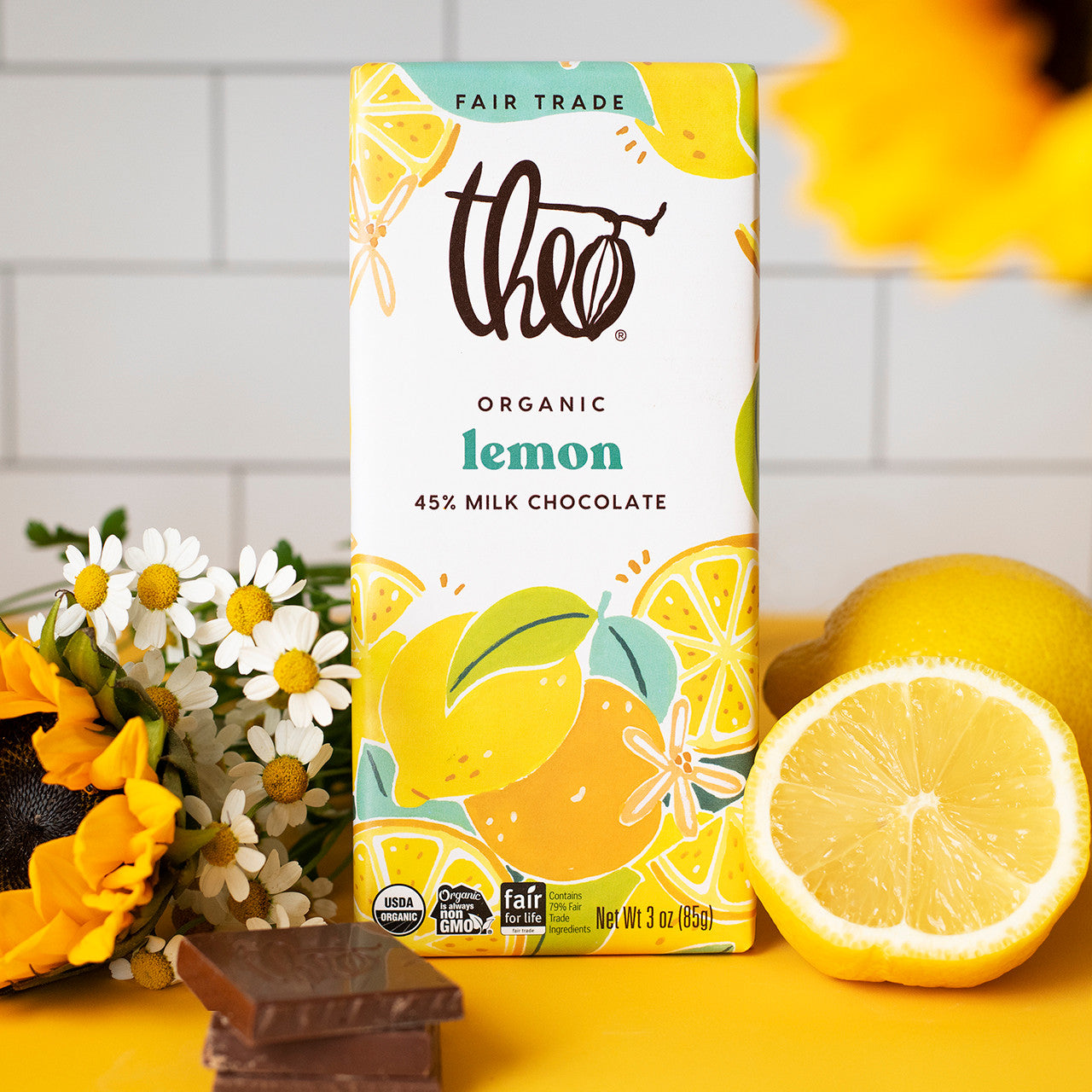 Theo Organic Lemon Milk Chocolate packaging with lemons and flowers on a yellow surface