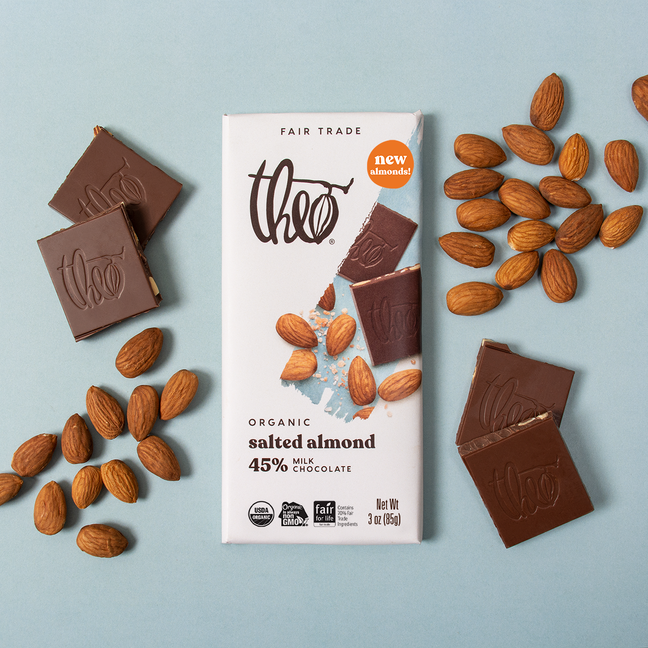 Theo organic salted almond milk chocolate bar with chocolate pieces and almonds on a light blue background