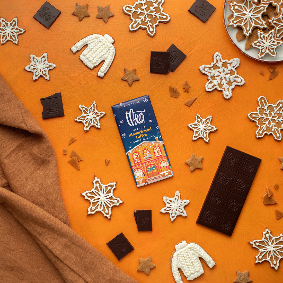 Theo gingerbread toffee dark chocolate bar surrounded by gingerbread cookies on an orange surface