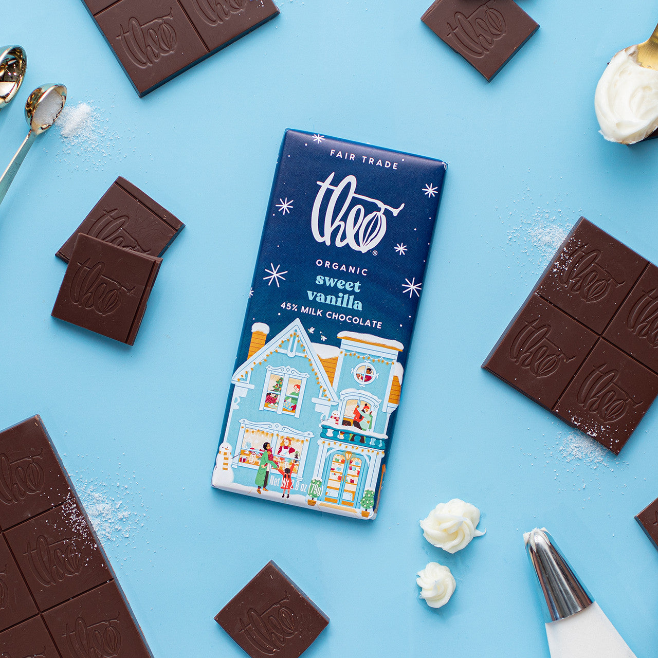 Theo Organic sweet vanilla milk chocolate bar on a blue background with chocolate pieces and decorative elements.