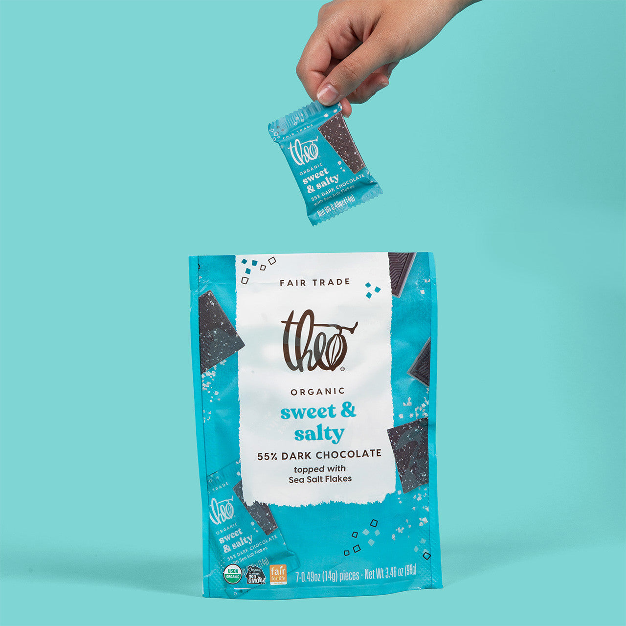 Theo Organic sweet &amp; salty dark chocolate packaging with a hand holding an individually wrapped chocolate piece against a teal background