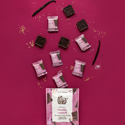 Theo Organic Vanilla Crunch dark chocolate bars with vanilla sea salt and packaging on a pink background
