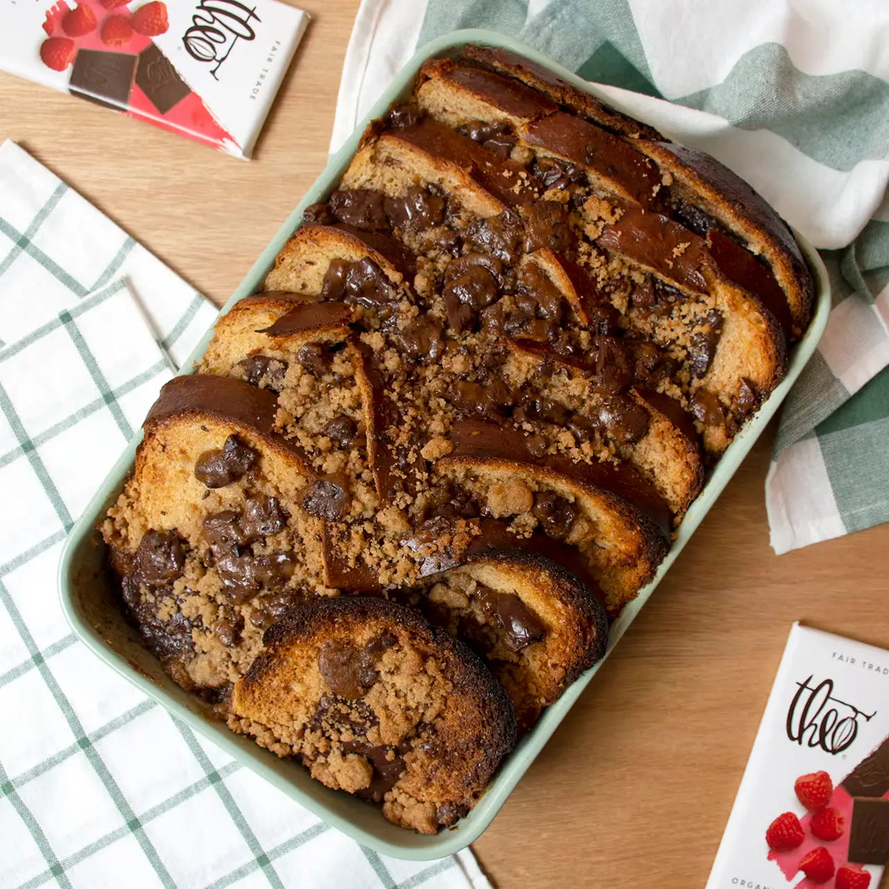Loaf of french toast bread sliced with chocolate on top in a green dish on a wooden table with chocolate bars.