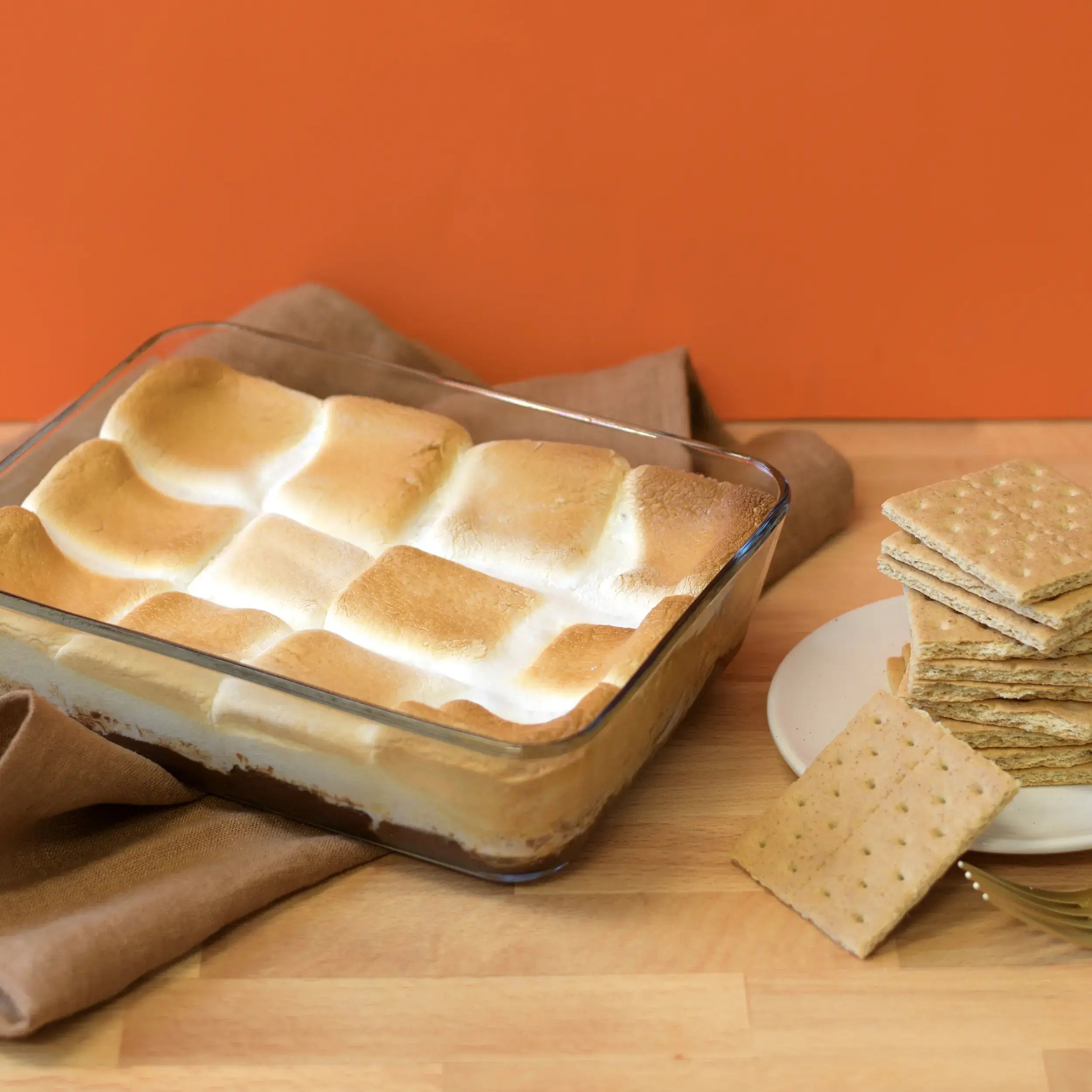 S'mores dessert in a glass dish with graham crackers on a wooden table.