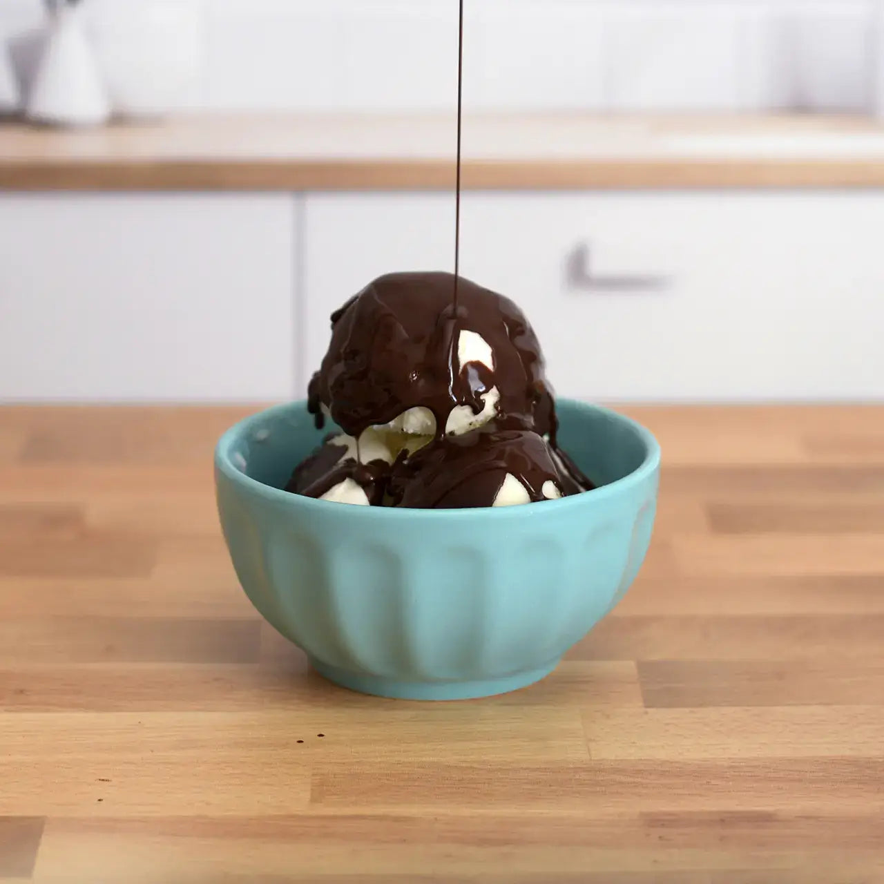 Blue bowl with ice cream and chocolate sauce on a wooden surface