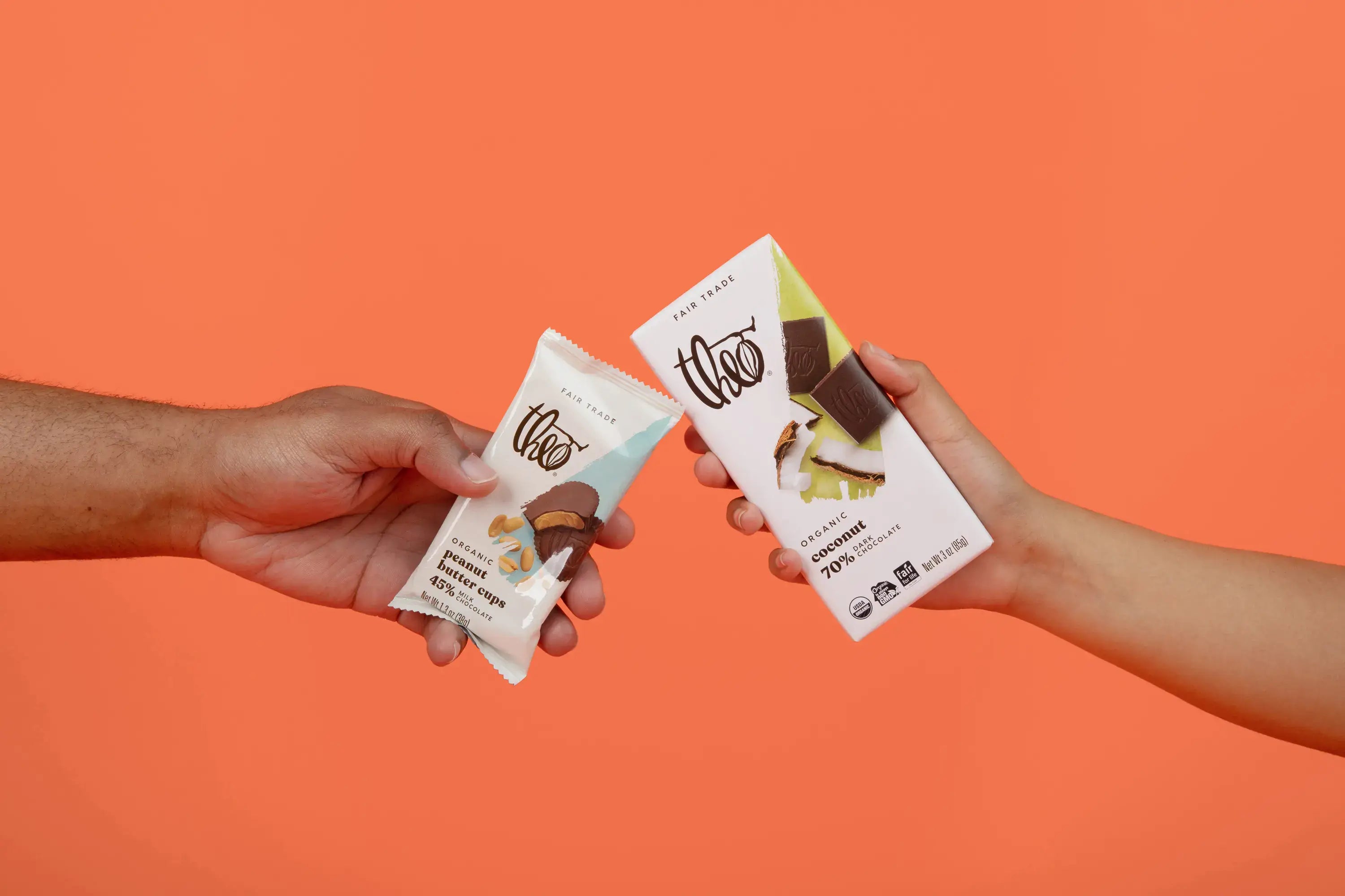 Two hands holding Theo chocolate bars against an orange background