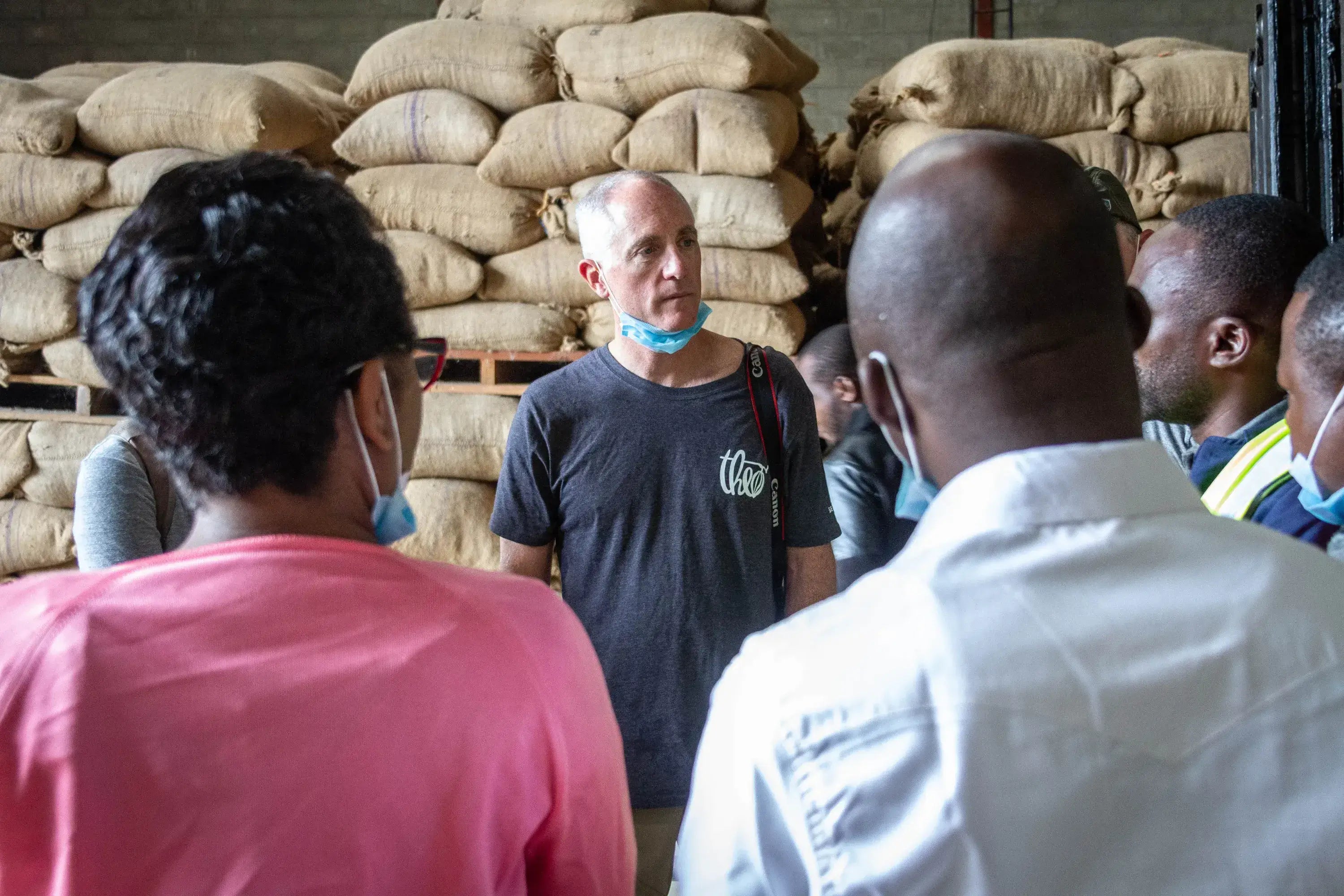 Group of people in a warehouse setting with stacked bags in the background